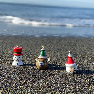 Snowman, Bear, and Santa Christmas Ornaments sitting on the beach shoreline